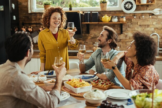 Mujer feliz sosteniendo un brindis mientras disfruta del almuerzo con sus amigos en casa.