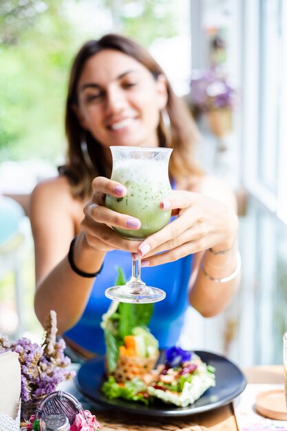 Mujer feliz sostiene té verde matcha japonés con hielo en vaso en café Mujer con bebida antioxidante saludable en verano lindo café