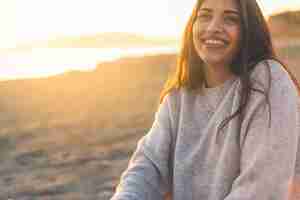 Foto gratuita mujer feliz en suéter sentado en la orilla del mar arena