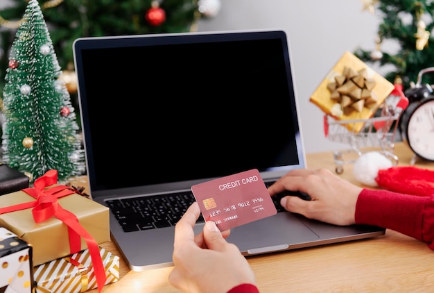 Mujer feliz con tarjeta de crédito haciendo compras online presentes en Navidad