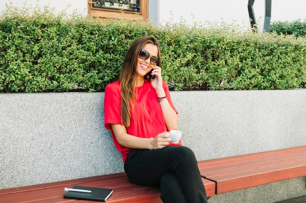 Mujer feliz con la taza de café que habla en smartphone