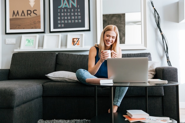 Mujer feliz con taza de café sentado y usando laptop