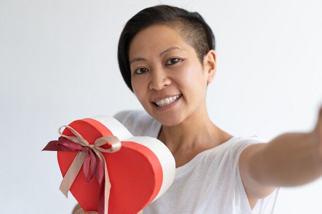 Mujer feliz tomando foto selfie con caja de regalo en forma de corazón