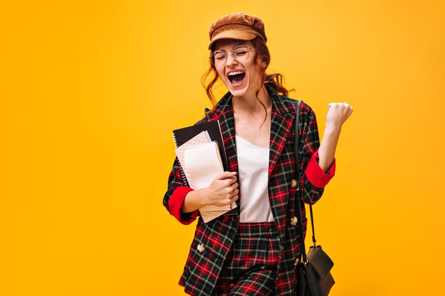 Mujer feliz en traje de moda emocionalmente posa con cuadernos en la pared naranja