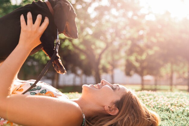 Mujer feliz tumbado en la hierba verde que sostiene dachshund en el parque