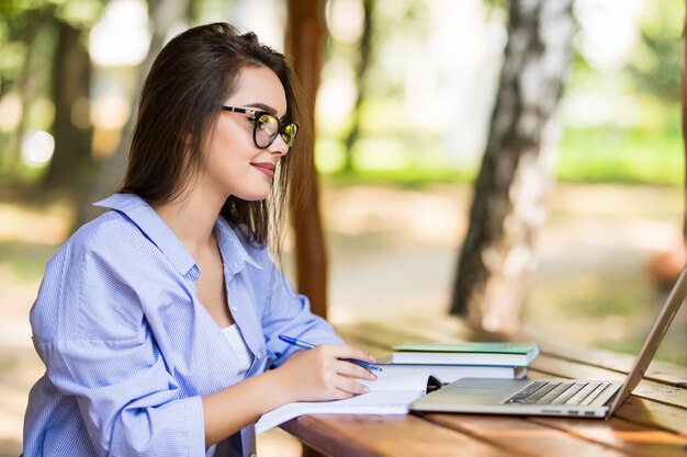 Mujer feliz usando una computadora portátil en una mesa del parque al final del día