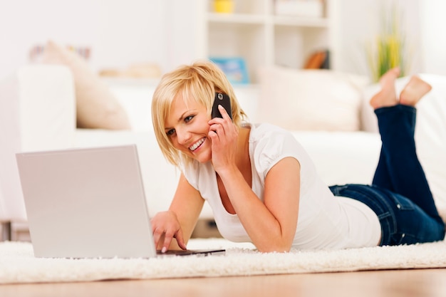 Mujer feliz usando laptop y hablando por teléfono móvil