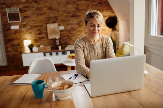 Mujer feliz usando laptop mientras trabaja en casa