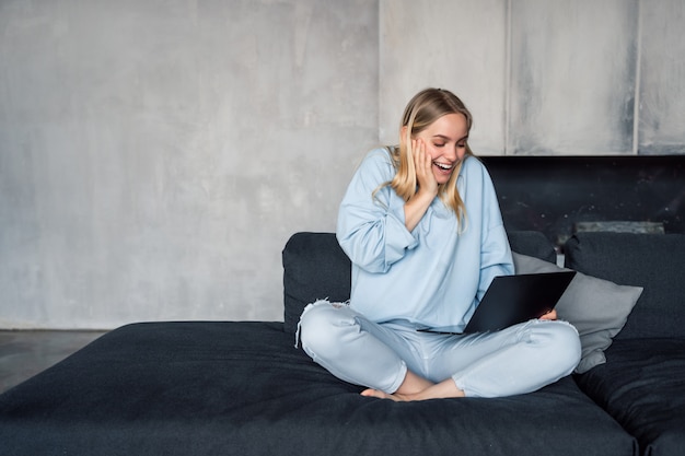 Mujer feliz usando laptop plateado mientras está sentado en el sofá