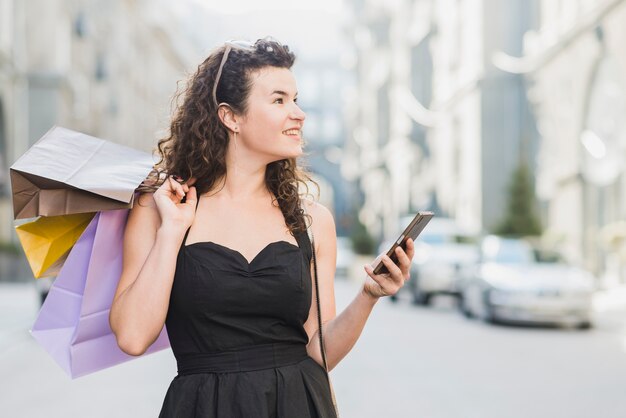 Mujer feliz con varios bolsos de compras que sostienen smartphone