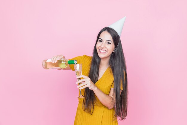 Mujer feliz vertiendo bebida en vidrio sobre fondo rosa