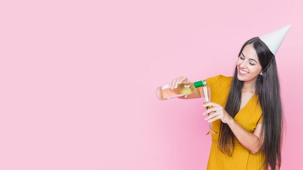 Mujer feliz vertiendo vino en vidrio sobre fondo rosa