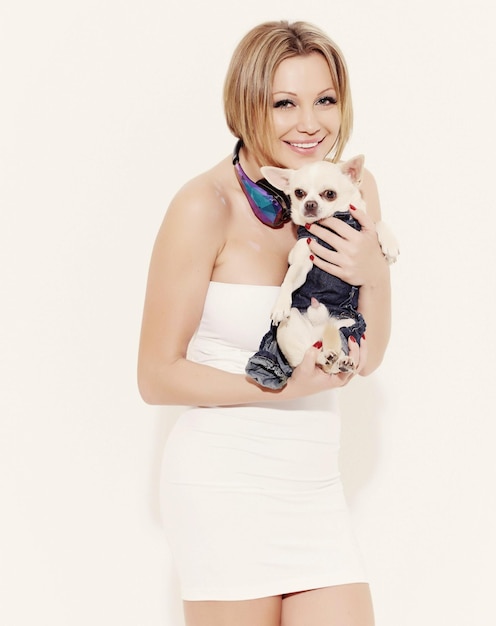 Una mujer feliz con un vestido blanco sosteniendo un pequeño perro chihuahua. Aislado en un fondo blanco.