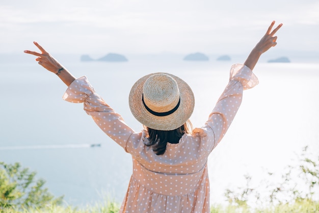 Mujer feliz en vestido lindo de verano y sombrero de paja de vacaciones con vistas exóticas tropicales