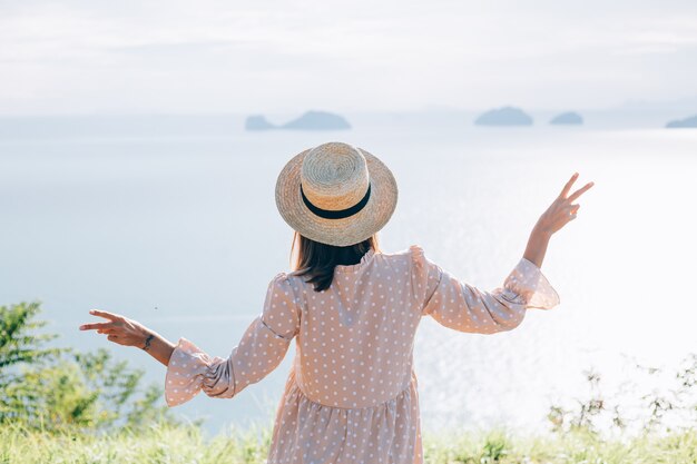 Mujer feliz en vestido lindo de verano y sombrero de paja de vacaciones con vistas exóticas tropicales