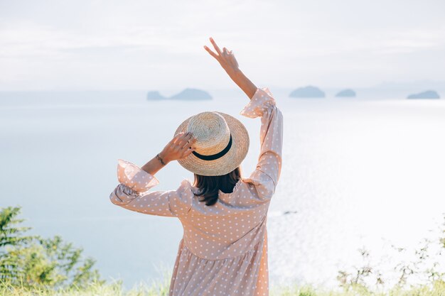 Mujer feliz en vestido lindo de verano y sombrero de paja de vacaciones con vistas exóticas tropicales