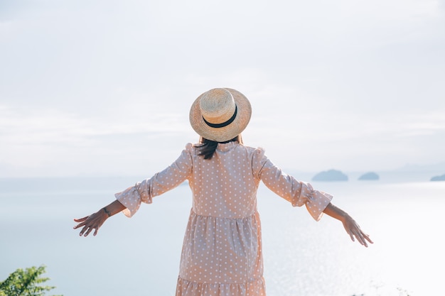 Mujer feliz en vestido lindo de verano y sombrero de paja de vacaciones con vistas exóticas tropicales