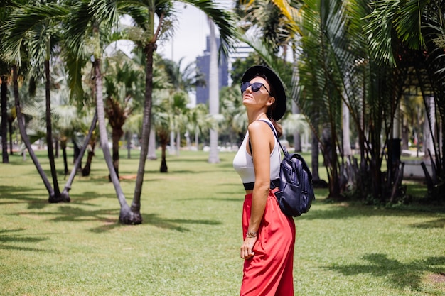 Mujer feliz viajar por Bangkok con mochila, disfrutando de un hermoso día soleado en un parque tropical en el campo de hierba verde