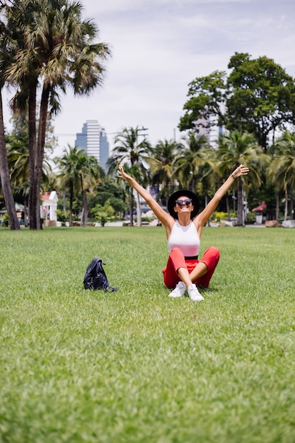 Mujer feliz viajar por Bangkok con mochila, disfrutando de un hermoso día soleado en un parque tropical en el campo de hierba verde