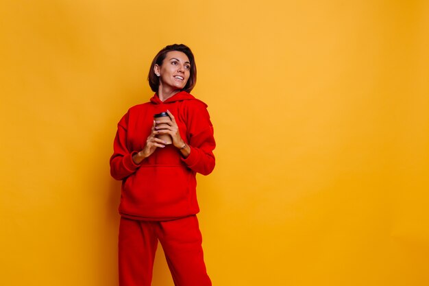 Mujer feliz vistiendo ropa abrigada de invierno, sudadera con capucha y pantalones, se calienta con una taza de café caliente