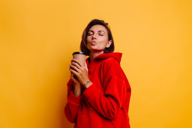 Mujer feliz vistiendo ropa de abrigo de invierno se calienta con una taza de café caliente