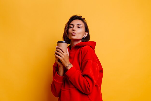 Mujer feliz vistiendo ropa de abrigo de invierno se calienta con una taza de café caliente