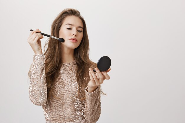 Mujer femenina mira en el espejo aplicar maquillaje