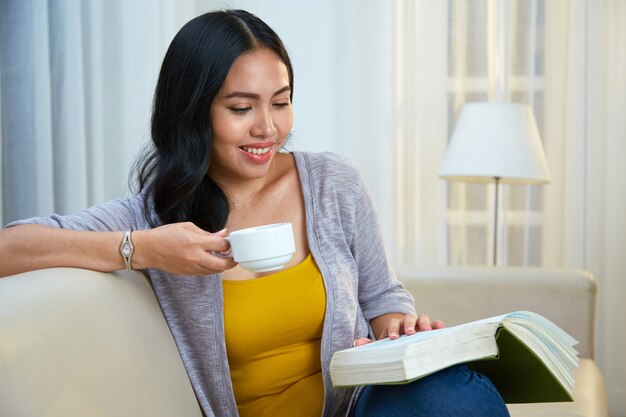 Mujer filipina bebiendo bebidas calientes y leyendo el libro