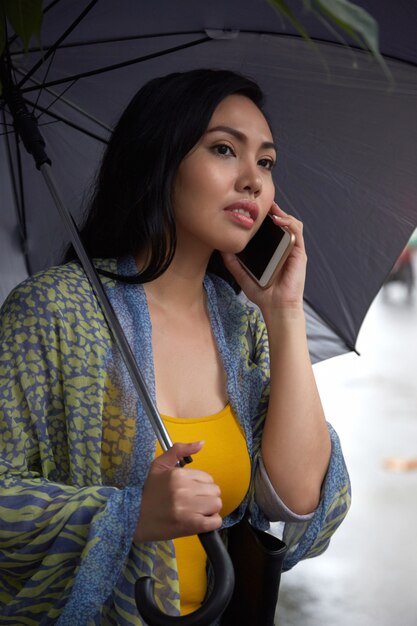 Mujer filipina con paraguas hablando por teléfono