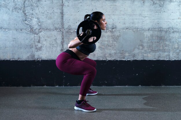 Mujer fitness deportivo en posición de cuclillas haciendo sentadillas y levantando pesas en el gimnasio