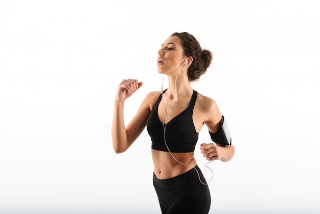 Mujer de fitness morena rizada concentrada corriendo y escuchando música