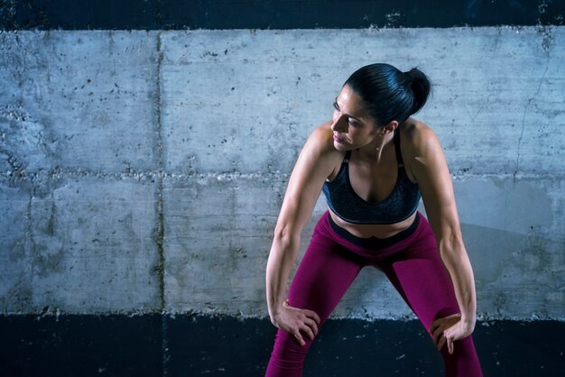 Mujer fitness en ropa deportiva apoyado en la pared de hormigón y mirando a un lado