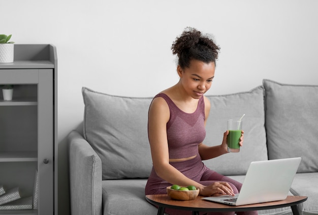 Mujer fitness tomando un jugo de fruta mientras usa una computadora portátil