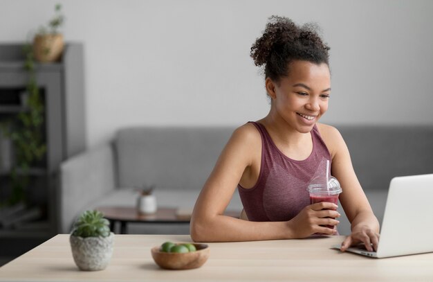 Mujer fitness tomando un jugo de fruta mientras usa una computadora portátil