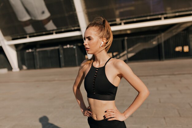 Mujer fitness urbano que se extiende en la plaza soleada del deporte. Colocar atleta trabajando afuera