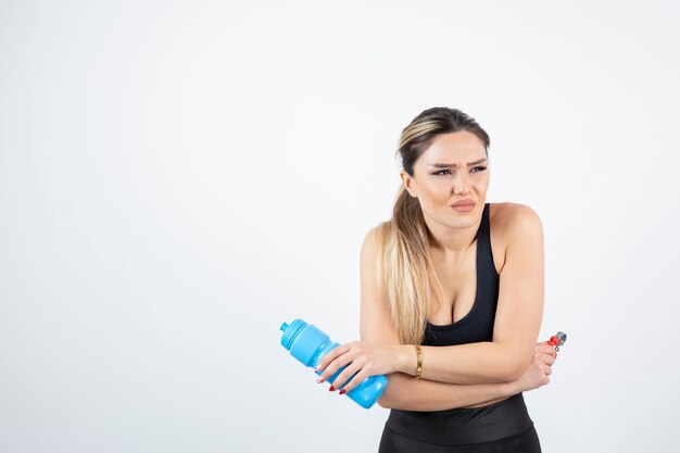 Mujer en forma rubia en top negro de pie y sosteniendo una botella de agua con expansor.