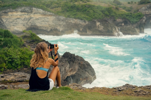 Mujer fotógrafa viajera fotografiando puntos de referencia en la cámara, Angel's Billabong beach, Nusa Penida Island, Bali, Indonesia.