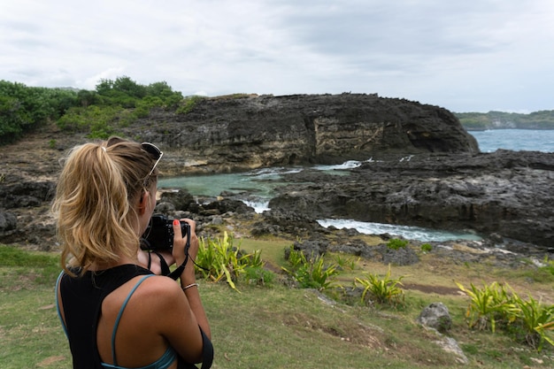 Foto gratuita mujer fotógrafa viajera fotografiando puntos de referencia en la cámara, angel's billabong beach, nusa penida island, bali, indonesia.