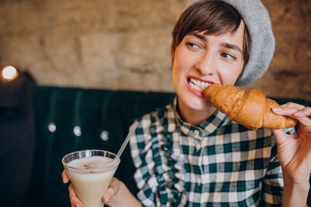 Mujer francesa en café bebiendo café con leche y comiendo croissant