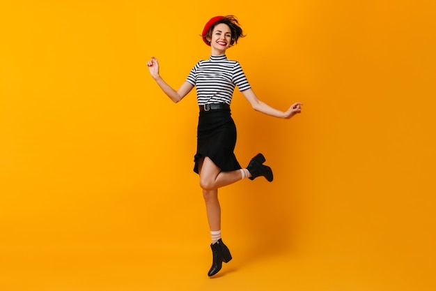 Mujer francesa con estilo alegre bailando en la pared amarilla