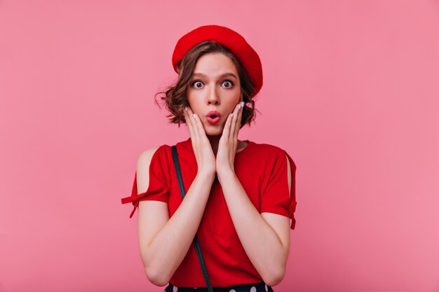 Mujer francesa de ojos oscuros expresando asombro. Retrato de niña glamorosa sorprendida en boina roja.