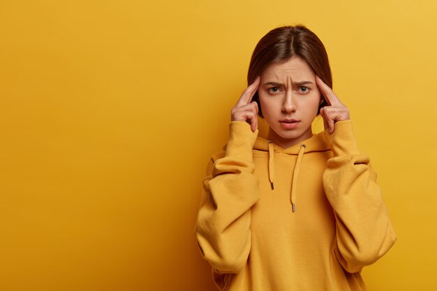 Mujer frustrada y disgustada toca las sienes con los dedos índices, se concentra en algo y piensa en una idea, intenta tomar una decisión seria, sufre de dolor de cabeza