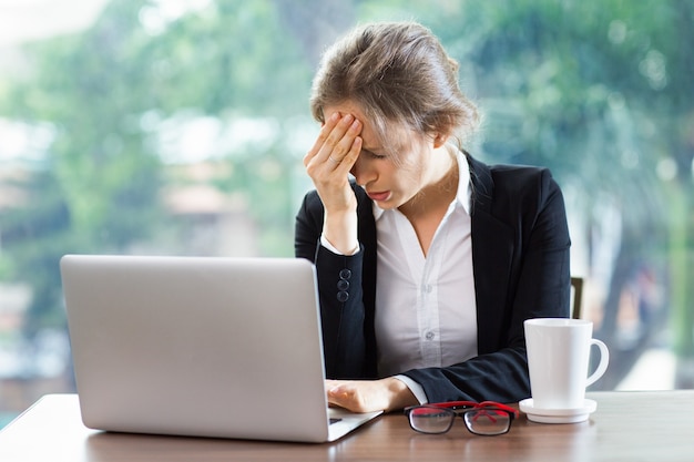 Mujer con un fuerte dolor de cabeza con un portátil y un café