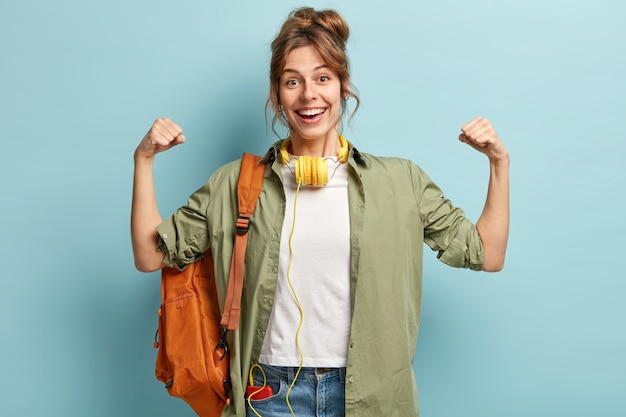 Mujer fuerte y poderosa levanta las manos y muestra los músculos, tiene una expresión alegre, usa auriculares