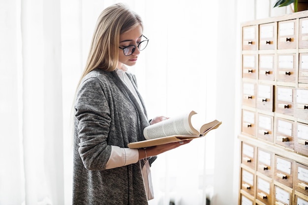 Foto gratuita mujer con gafas leyendo cerca de la ventana