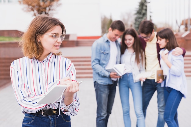 Mujer en gafas de pie y sosteniendo el cuaderno en las manos