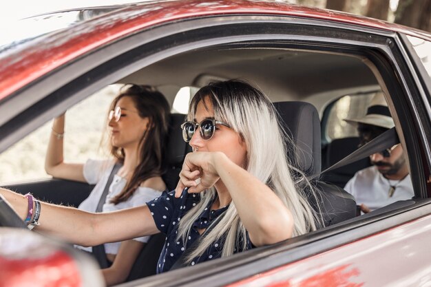 Mujer con gafas de sol conduciendo coche con sus amigos