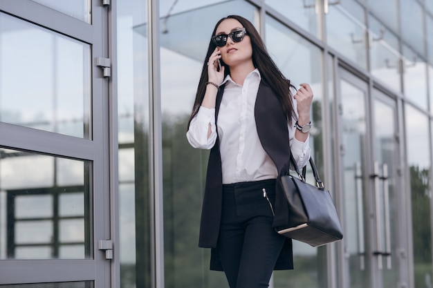 Foto gratuita mujer con gafas de sol hablando por teléfono con unas cristaleras gigantes detrás