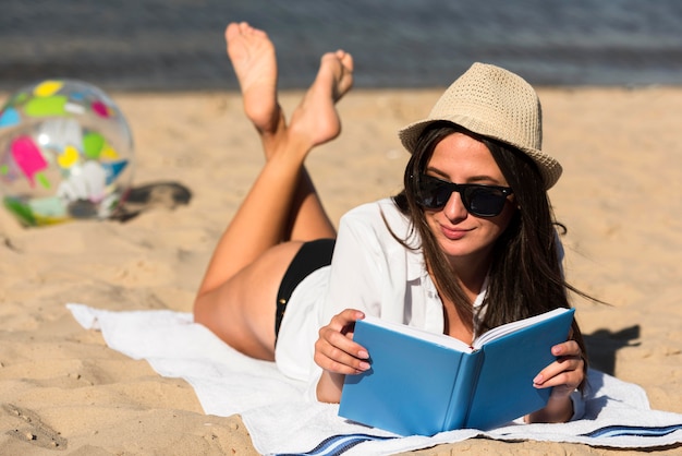 Mujer con gafas de sol leyendo un libro en la playa.