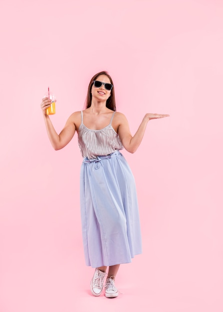 Mujer en gafas de sol de pie y sosteniendo el vaso de jugo